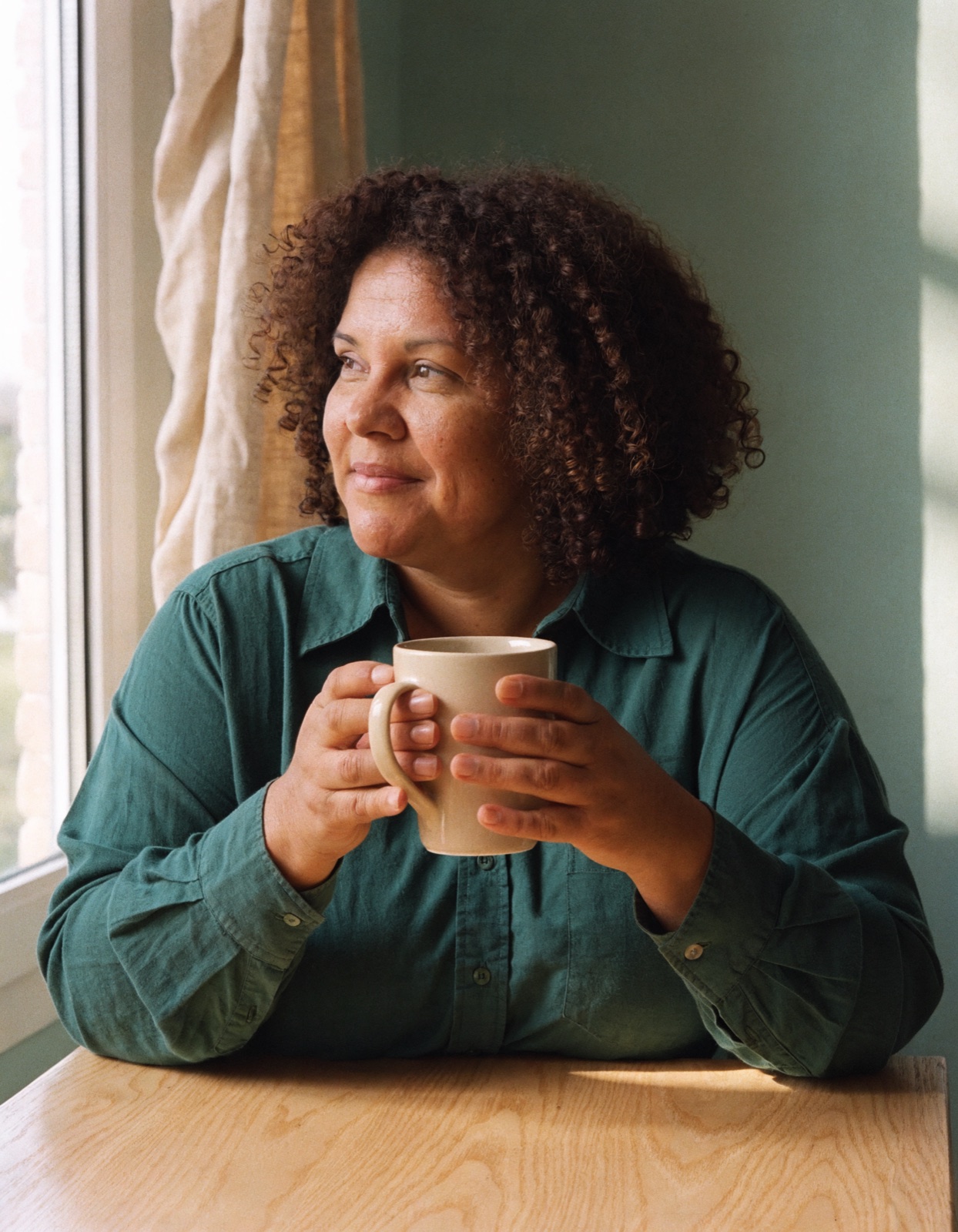 Mulher sentada perto da janela, segurando uma caneca.